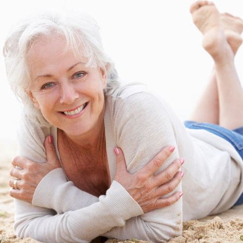 An older woman lays in the sand at the beach