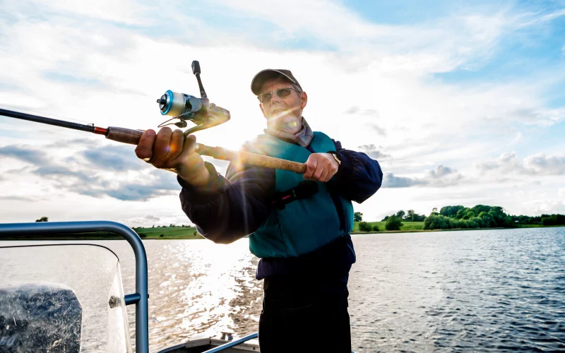 Senior man fishing on boat on the water at sunset